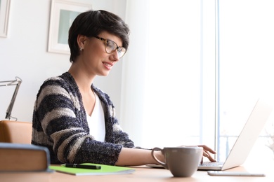 Photo of Young woman working with laptop at desk. Home office