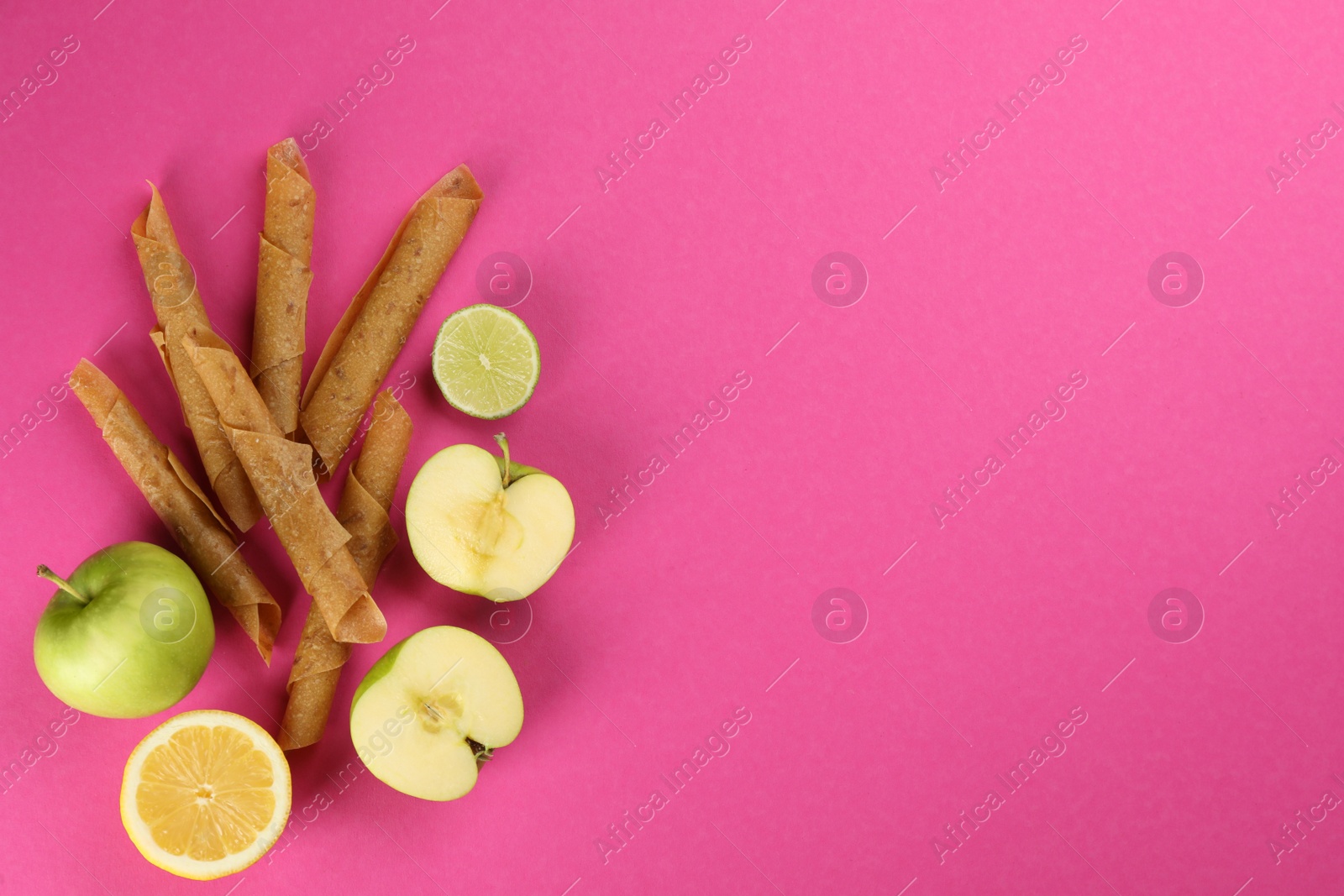 Photo of Delicious fruit leather rolls, lemon, lime and apples on pink background, flat lay. Space for text