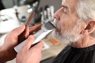 Professional barber trimming client's mustache in barbershop