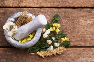 Photo of Mortar with pestle, dry flowers and ears of wheat on wooden table, flat lay. Space for text