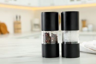Photo of Salt and pepper mills on white marble table in kitchen. Space for text
