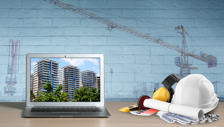 Image of Modern laptop with engineer equipment on table and construction crane. Double exposure 