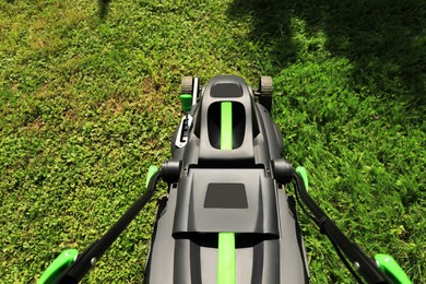 Photo of Cutting green grass with lawn mower in garden, above view