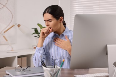 Photo of Woman coughing at table in office. Cold symptoms