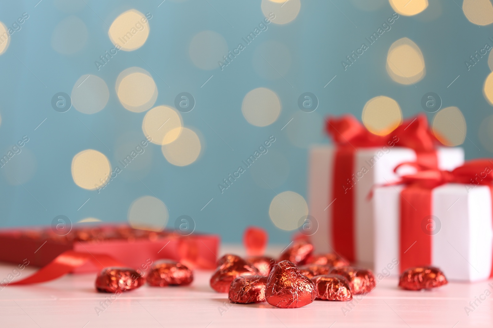 Photo of Heart shaped chocolate candies on pink table against blurred lights, space for text. Valentines's day celebration