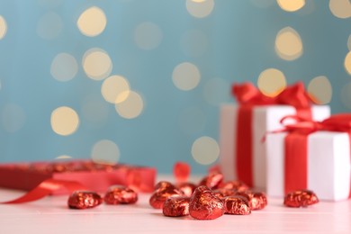 Heart shaped chocolate candies on pink table against blurred lights, space for text. Valentines's day celebration