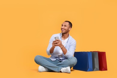 Photo of Happy African American man with shopping bags and smartphone on orange background