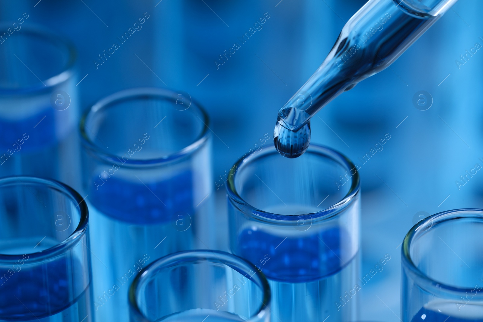 Photo of Dripping reagent into test tube on light blue background, closeup. Laboratory analysis