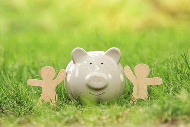 Photo of Cute piggy bank and wooden people on green grass in park