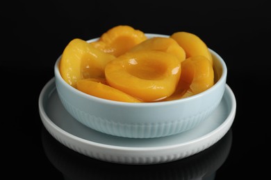 Photo of Canned peach halves in bowl on black background