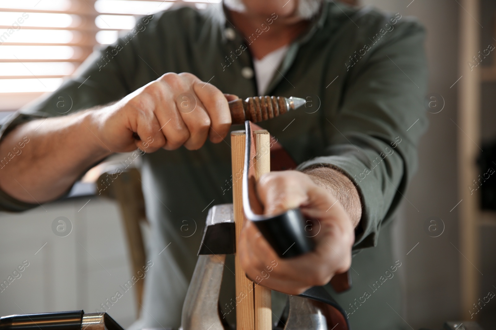Photo of Man burnishing edges of leather belt in workshop, closeup