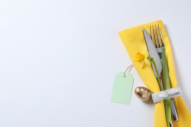 Photo of Cutlery set, Easter egg and narcissus on white background, flat lay with space for text. Festive table setting