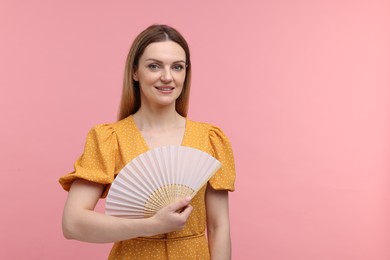 Happy woman with hand fan on pink background, space for text