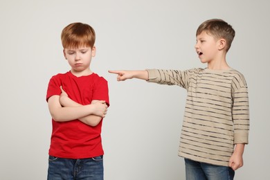 Boy laughing and pointing at upset kid on light grey background. Children's bullying