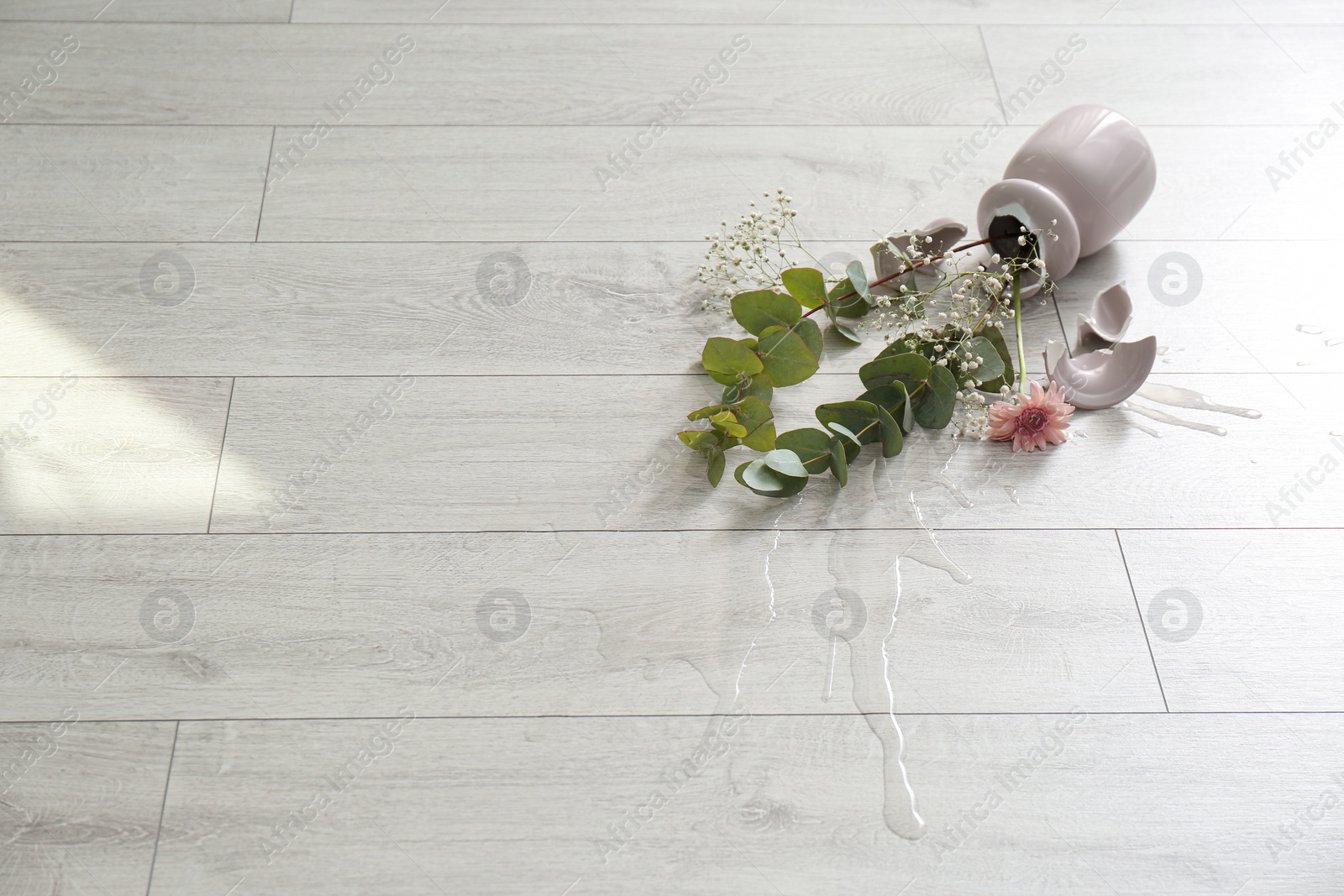 Photo of Broken pink ceramic vase and bouquet on wooden floor. Space for text