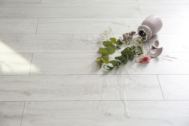 Broken pink ceramic vase and bouquet on wooden floor. Space for text