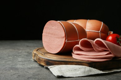 Photo of Board with tasty boiled sausages on dark textured table against black background, closeup. Space for text