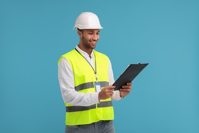 Photo of Engineer in hard hat holding clipboard on light blue background