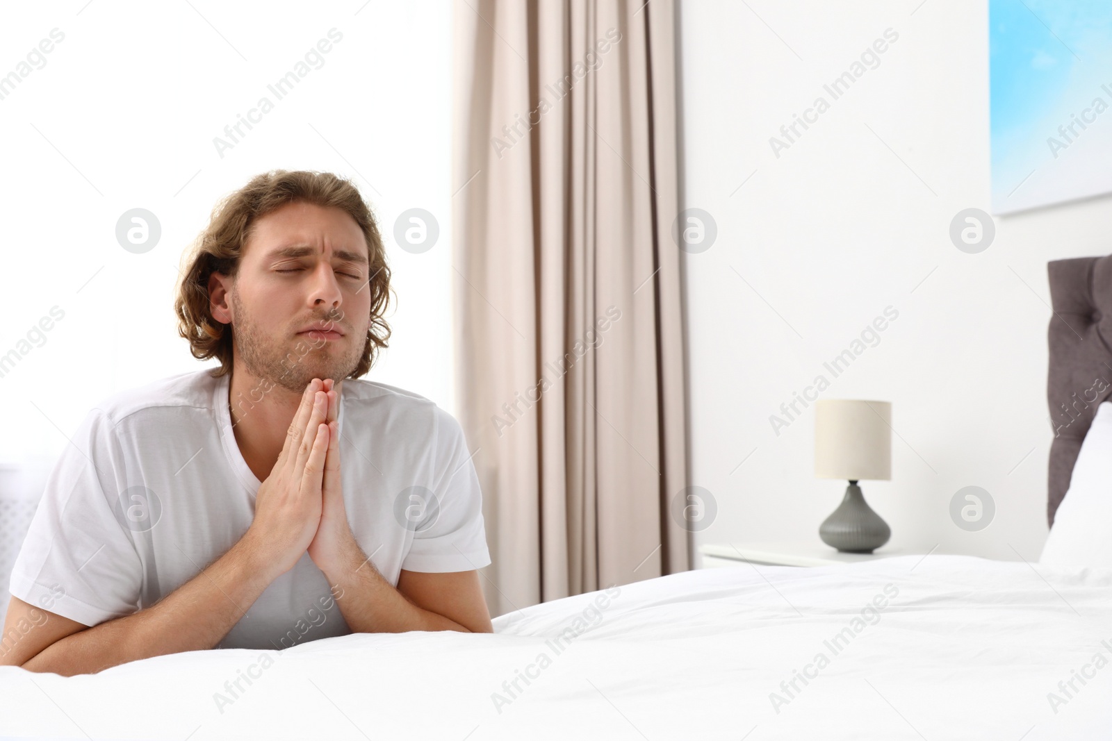 Photo of Handsome young man saying bedtime prayer at home. Space for text