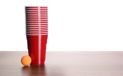 Photo of Plastic cups and ball for beer pong on wooden table against white background