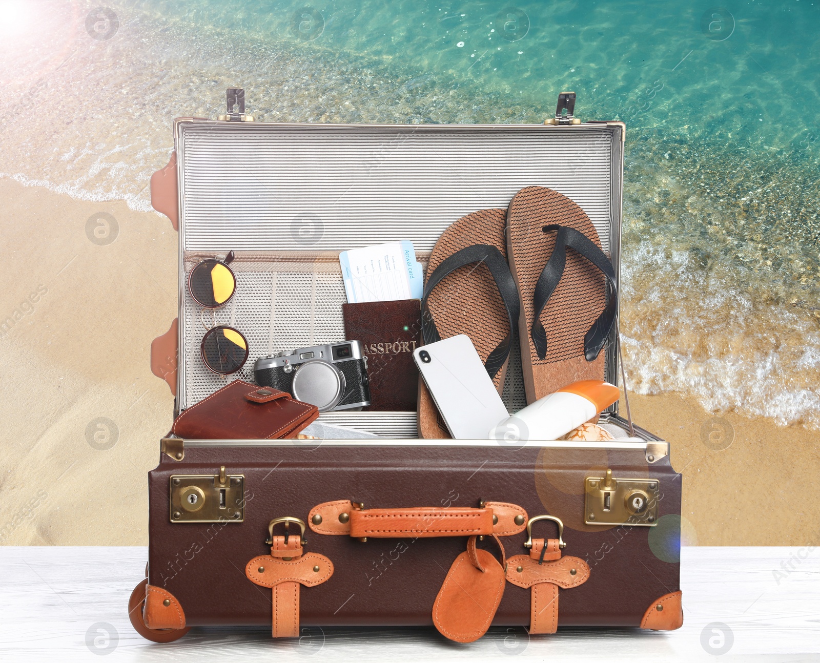 Image of Suitcase with different beach objects on wooden table near sea