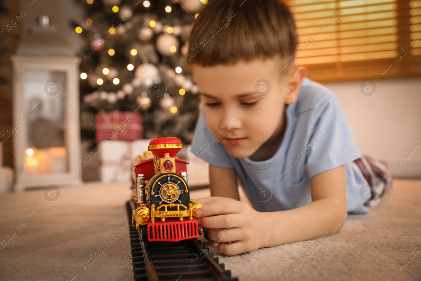 Photo of Little boy playing with colorful toy in room decorated for Christmas, focus on train