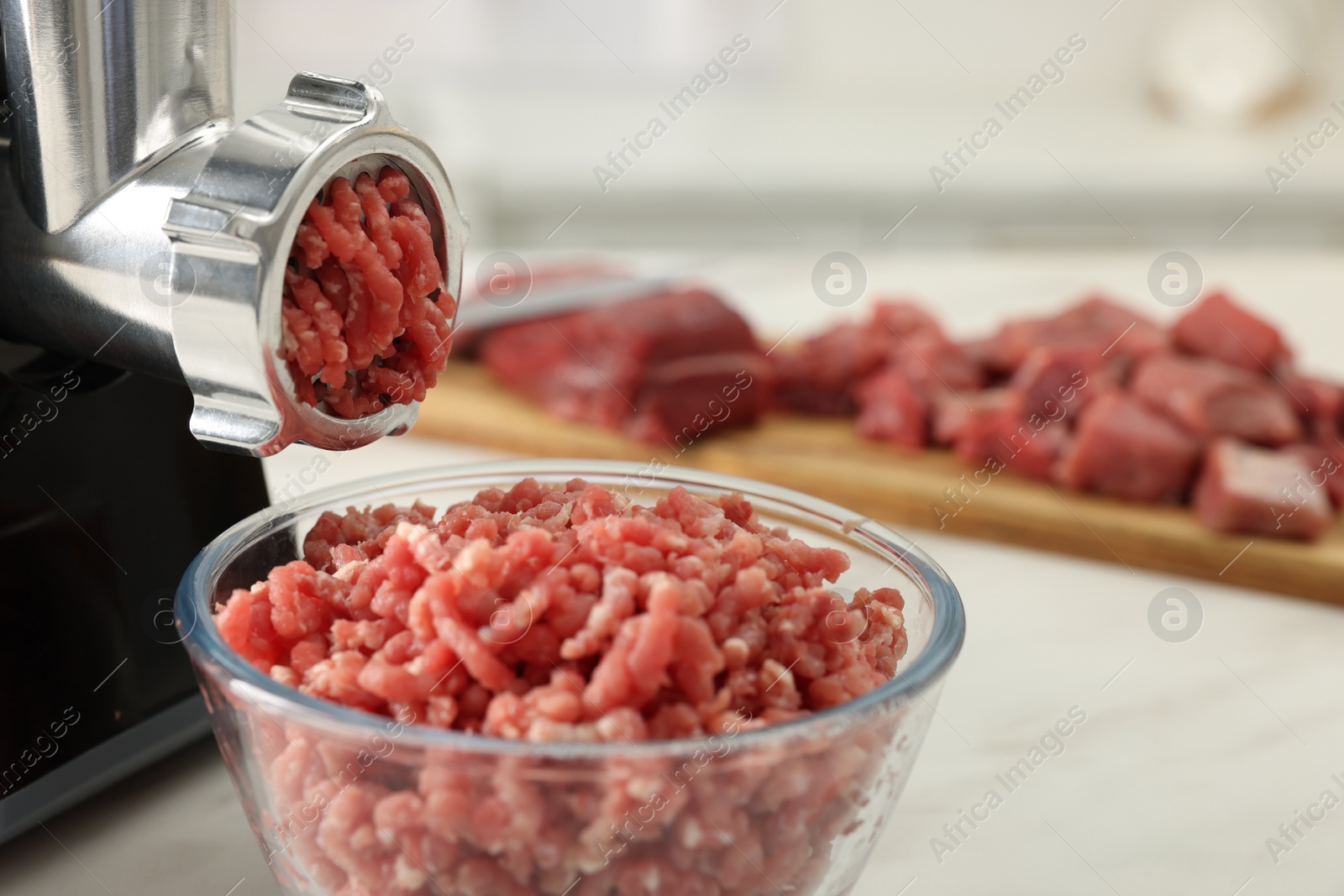 Photo of Electric meat grinder with minced beef on white table, closeup