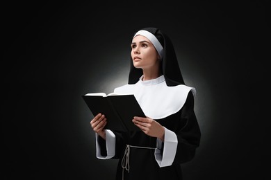 Young nun with Bible on black background