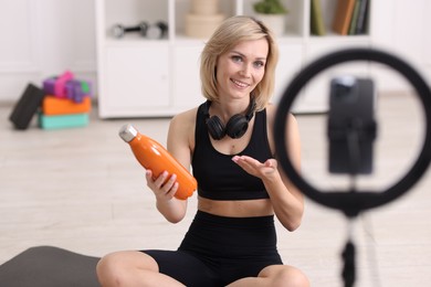 Photo of Smiling sports blogger holding bottle while streaming online fitness lesson at home