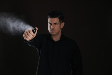 Photo of Man using pepper spray against black background, focus on hand