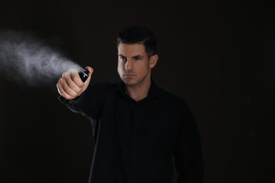 Man using pepper spray against black background, focus on hand