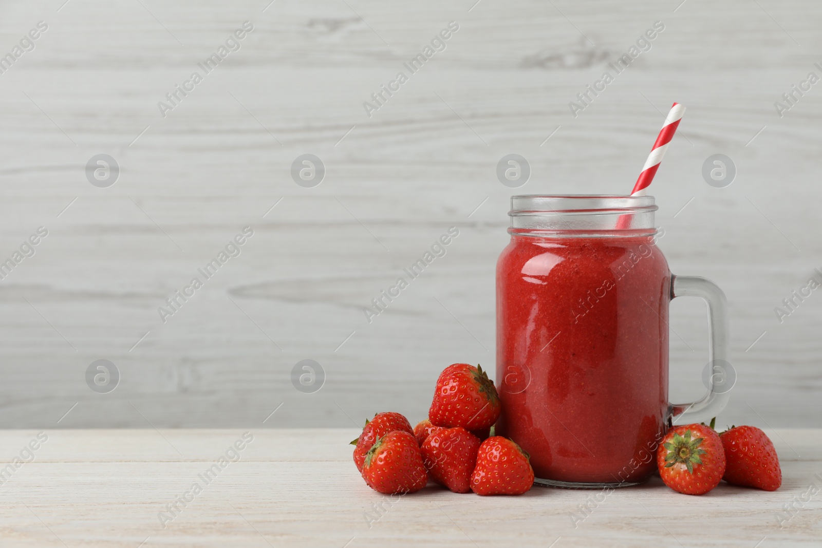 Photo of Mason jar with delicious strawberry smoothie and fresh berries on white wooden table. Space for text