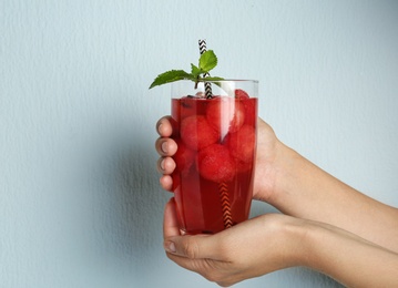 Woman holding glass of watermelon ball cocktail with mint against light blue background, closeup