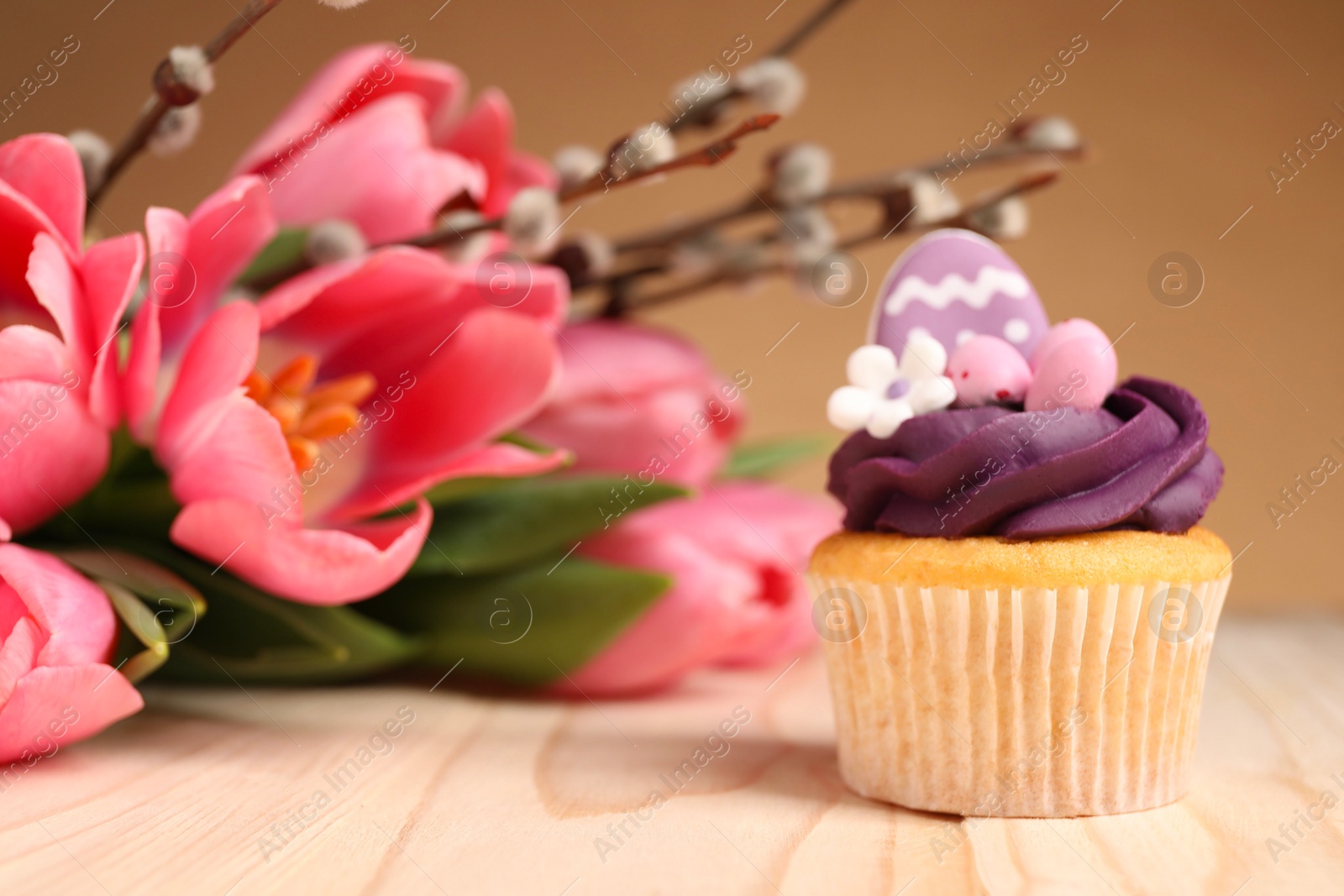 Photo of Tasty decorated Easter cupcake, flowers and willow branches on wooden table