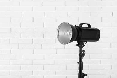 Photo of Professional studio flash light with reflector near white brick wall, space for text. Photography equipment