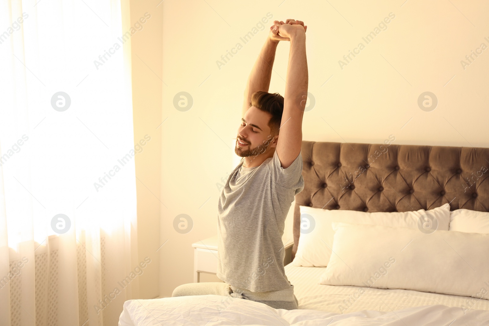 Photo of Young man stretching on bed at home. Lazy morning