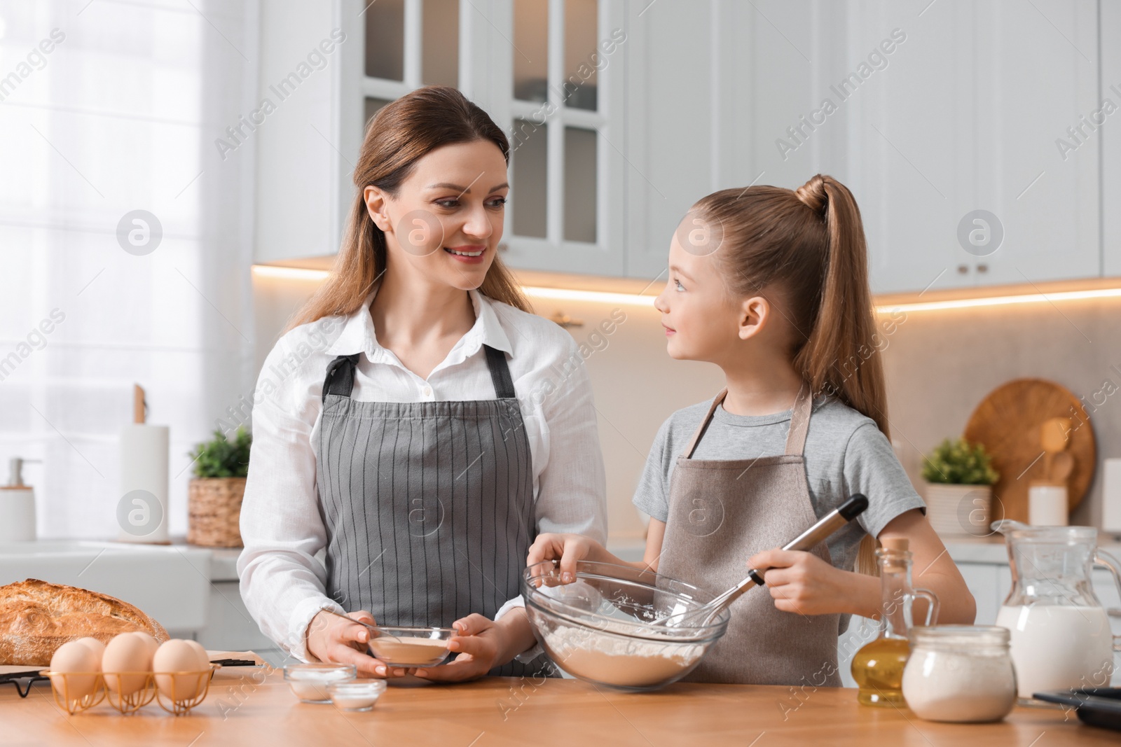 Photo of Making bread. Mother and her daughter putting flour and dry yeast into bowl at wooden table in kitchen