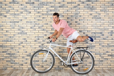 Photo of Handsome young hipster man riding bicycle near brick wall