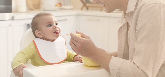 Image of Father feeding his cute little baby in kitchen. Banner design