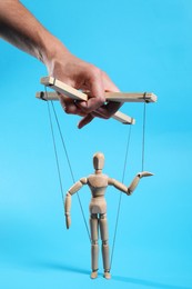 Photo of Man pulling strings of puppet on light blue background, closeup