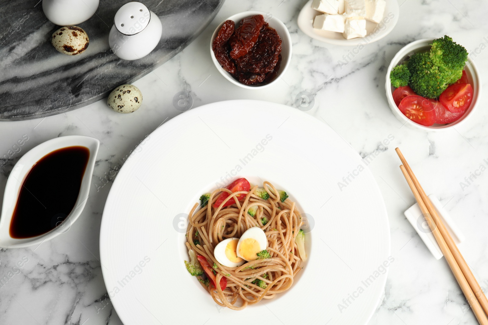 Photo of Tasty buckwheat noodles served on white marble table, flat lay