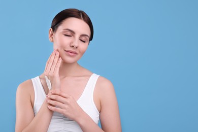 Beautiful woman with smear of body cream on her hand against light blue background, space for text