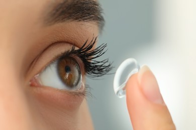 Photo of Woman putting contact lens in her eye on blurred background, closeup