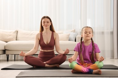 Photo of Mother with daughter in sportswear meditating together at home. Harmony and zen