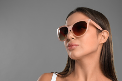 Photo of Beautiful young woman wearing sunglasses on grey background. Space for text