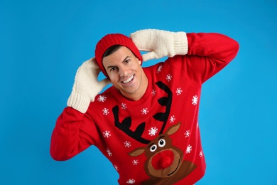 Photo of Happy man in Christmas sweater, mittens and hat on blue background