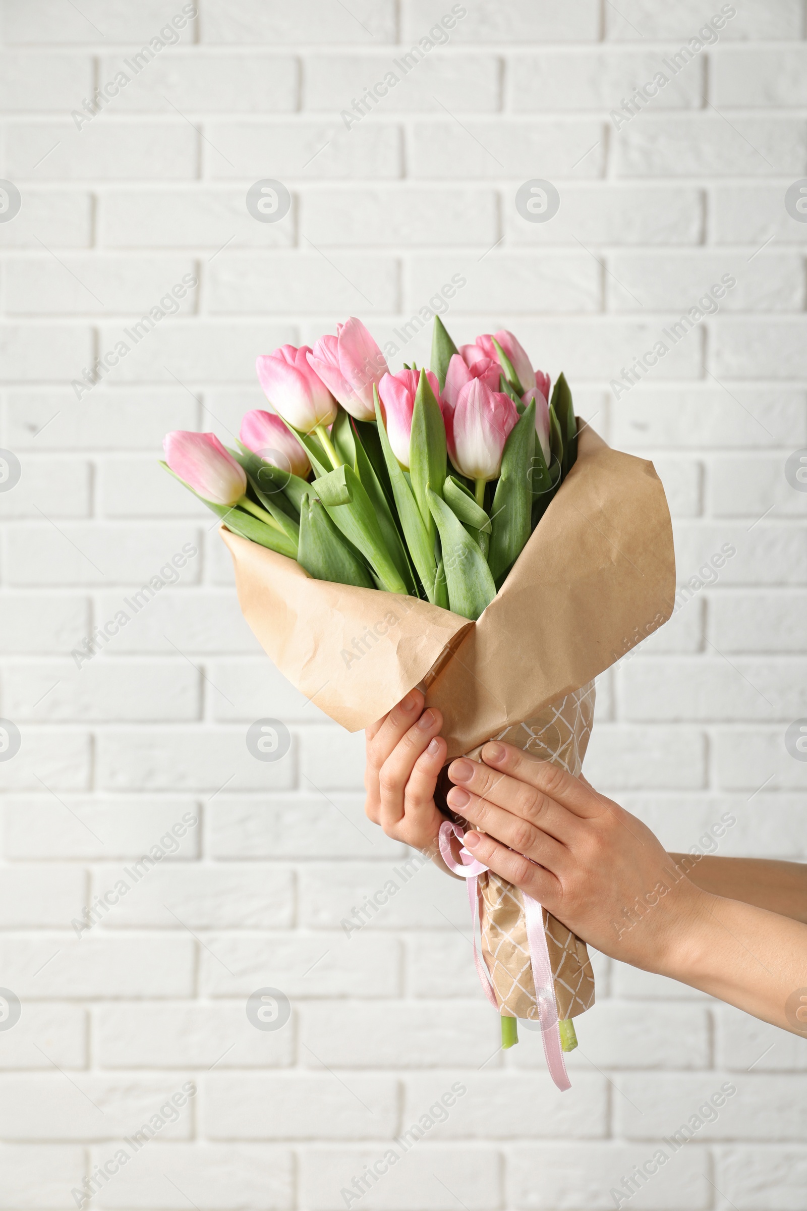 Photo of Girl holding bouquet of beautiful spring tulips near brick wall, closeup. International Women's Day