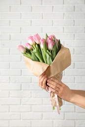 Girl holding bouquet of beautiful spring tulips near brick wall, closeup. International Women's Day