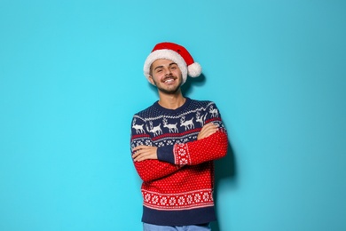 Young man in Christmas sweater and hat on color background