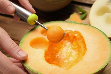 Woman making melon balls at wooden table, closeup